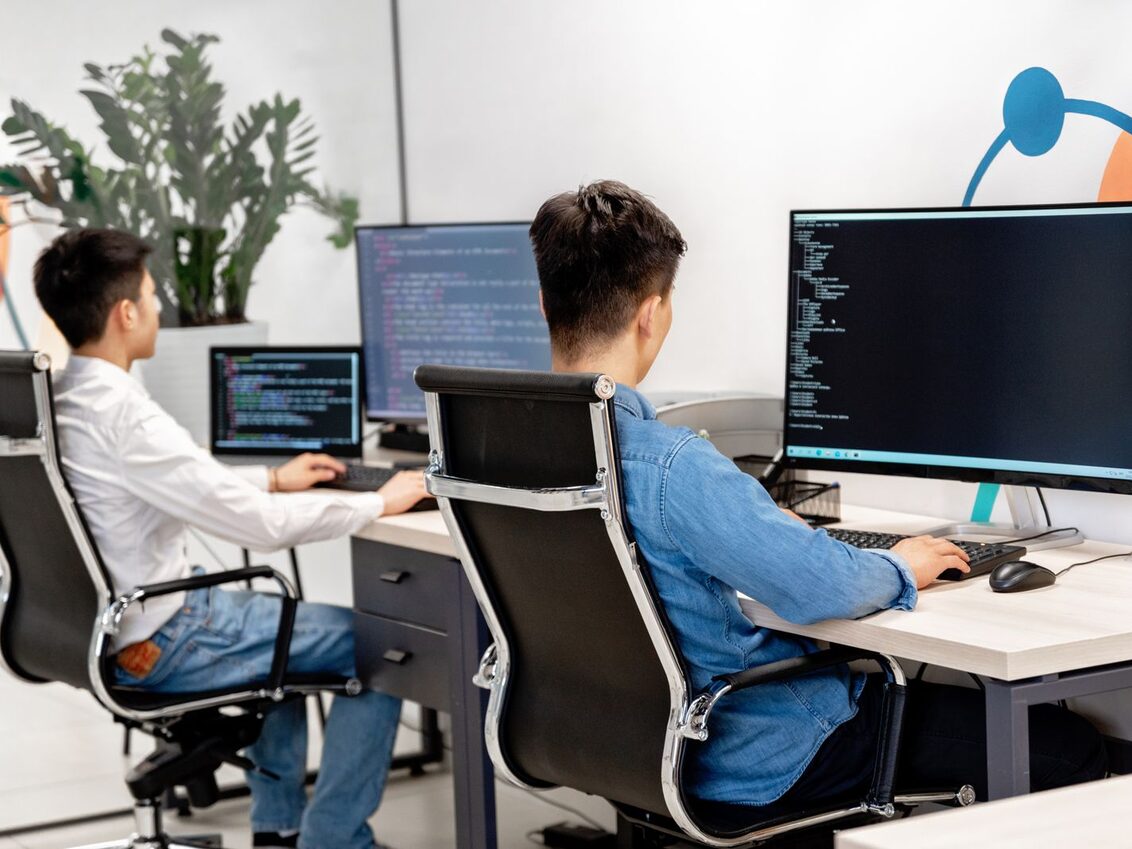Two developers working at monitors of code in a bright office